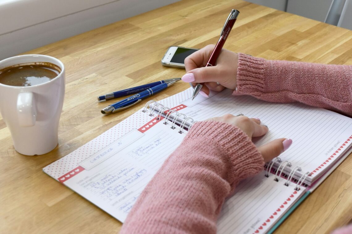 Person skriver noter i en notesbog ved et bord med en kop kaffe