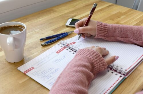 Person skriver noter i en notesbog ved et bord med en kop kaffe