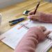 Person skriver noter i en notesbog ved et bord med en kop kaffe