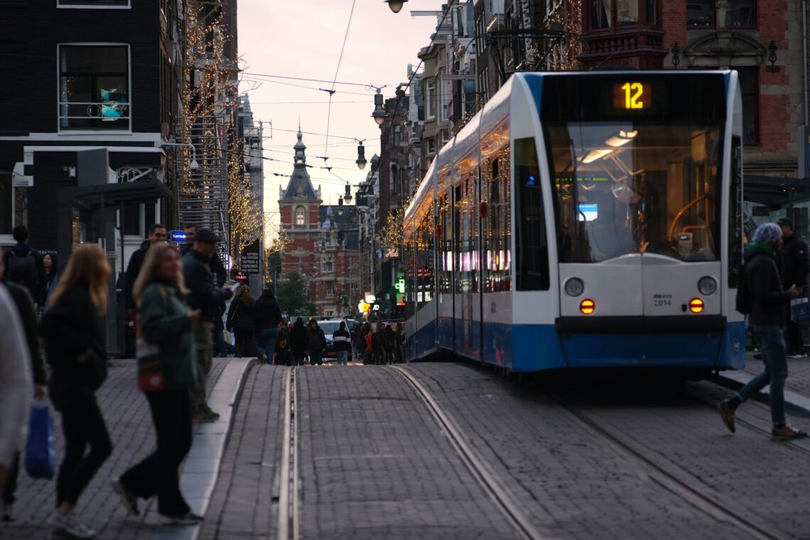 Blå og hvid letbane kører gennem en bygade med kontorbyggeri i dagslys