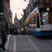 Blå og hvid letbane kører gennem en bygade med kontorbyggeri i dagslys